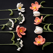 Handmade crochet tulips and small white flowers with green stems arranged on a black background